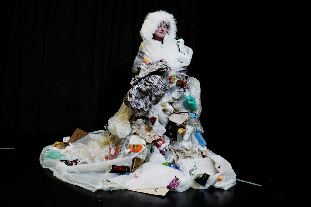 Die Schauspielerin Antje Töpfer ist in einen Königsmantel aus Müll eingehüllt, und schaut in die Kamera.