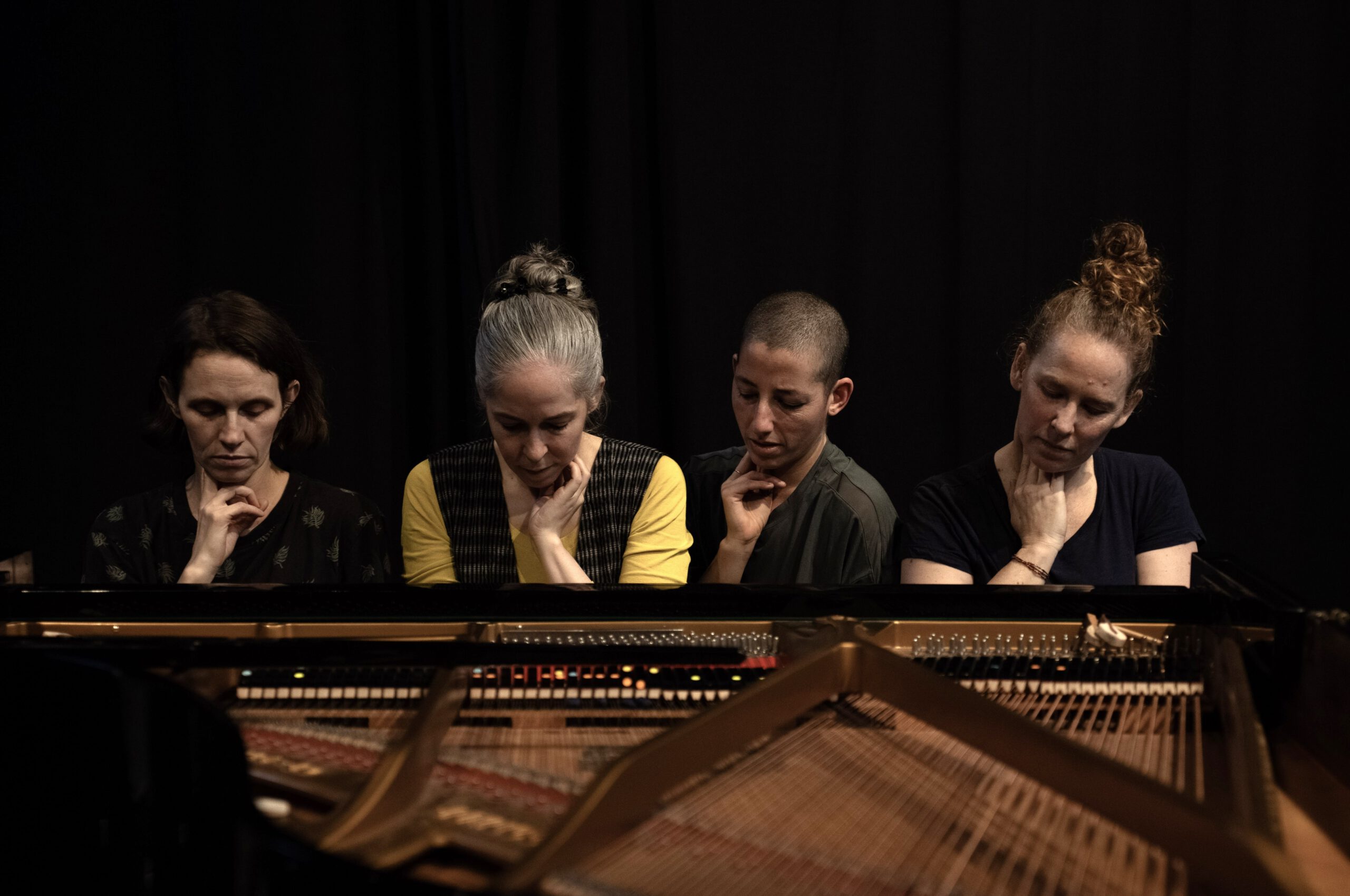 vier FLINTA Personen hinter einem Klavier. Man sieht nur ihre Oberkörper, sie blicken auf die Tasten.